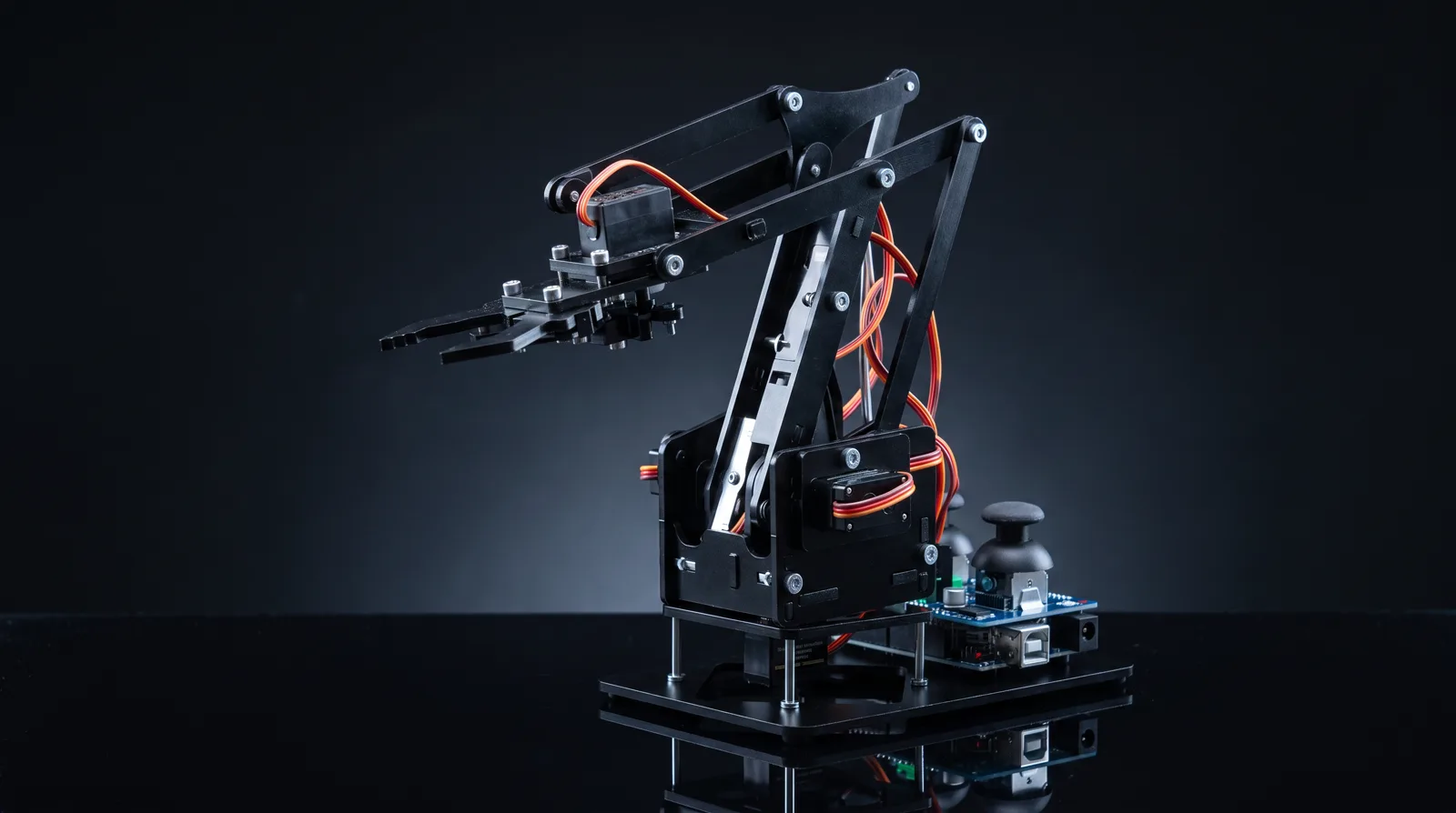 The RA01 robotic arm: black laser-cut acrylic, four servos with orange cables, dual-joystick controller base